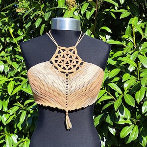 May include: A crocheted halter top with a geometric pattern in shades of brown and beige. The top has a tassel at the bottom.