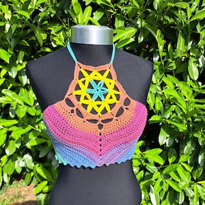 May include: A rainbow crochet halter top with a geometric design in the center. The top is made with a variety of colors, including pink, orange, yellow, green, blue, and purple.