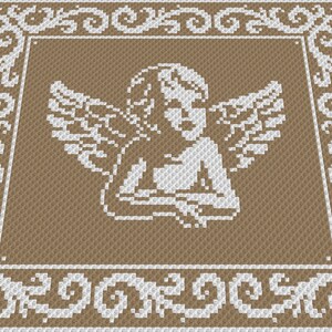 May include: A white angel with wings is embroidered on a brown fabric background. The angel is surrounded by a white decorative border.