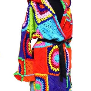 May include: A vibrant, handmade crochet robe featuring a patchwork design in a spectrum of colors including red, orange, yellow, green, blue, and purple. The robe has a hood, long sleeves, and a black belt. The crochet work is detailed and intricate.