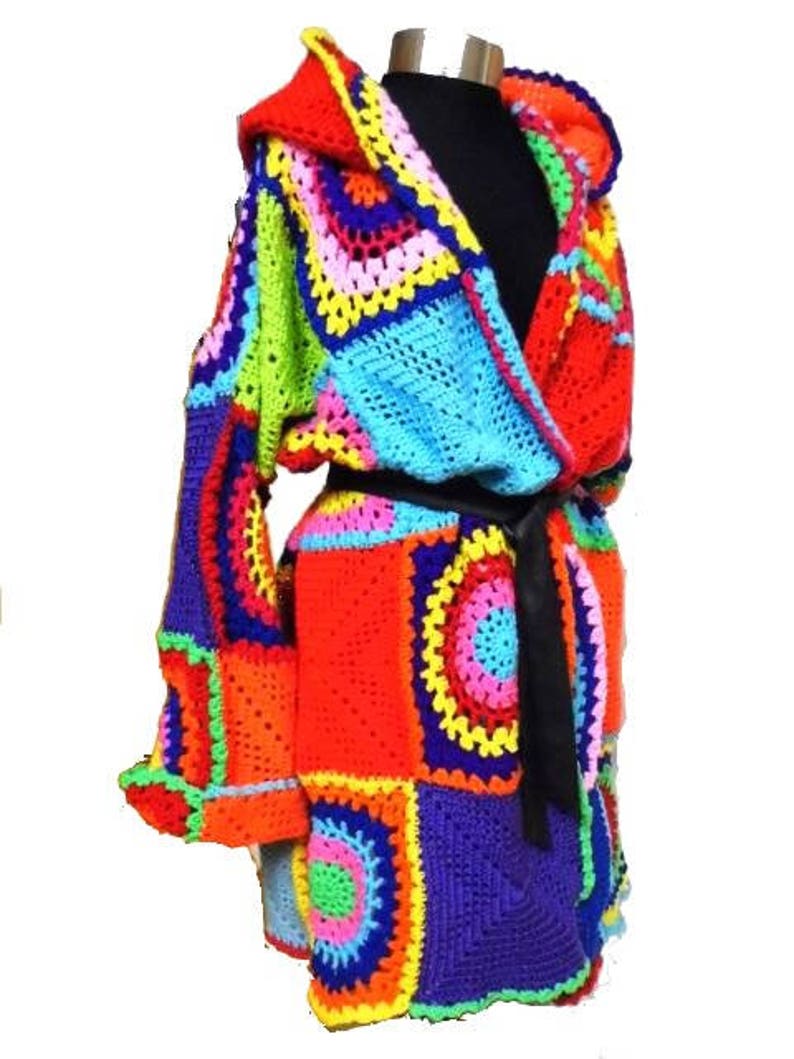 May include: A vibrant, handmade crochet robe featuring a patchwork design in a spectrum of colors including red, orange, yellow, green, blue, and purple. The robe has a hood, long sleeves, and a black belt. The crochet work is detailed and intricate.