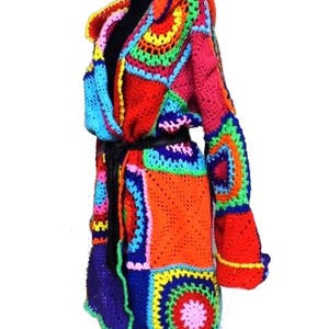 May include: A vibrant, handmade crochet coat in a patchwork design. The coat features a mix of bright colors including red, orange, blue, green, and pink. It has long sleeves and a hood, with a black belt cinching the waist. The coat is displayed on a mannequin.