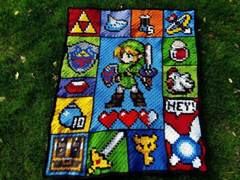 以下が含まれることがあります： ゼルダの伝説のビデオゲームシリーズのキャラクターとアイテムを特徴とするピクセルデザインのクロシェブランケット。ブランケットは、緑、青、赤、黄、黒など、さまざまな色で作られています。ブランケットには、ゲームの主人公であるリンクのピクセル画像が描かれており、剣と盾を持っています。ブランケットには、トライフォース、ハートコンテナ、ルピーなど、ゲームの他の象徴的なアイテムも描かれています。
