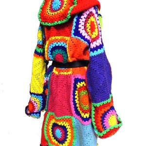 May include: A vibrant, patchwork crochet jacket in a variety of colors, including red, yellow, blue, and green. The jacket features a hood and a unique, geometric design. The sleeves are long and the jacket has a skirt-like bottom.