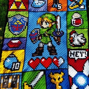 以下が含まれることがあります： ゼルダの伝説のビデオゲームシリーズから、さまざまなピクセル化されたキャラクターとオブジェクトをフィーチャーした、かぎ針編みの毛布。毛布は、緑、青、赤、黄、白など、さまざまな色で作られています。キャラクターとオブジェクトには、リンク、剣、ハート、爆弾、盾、トライフォースが含まれます。