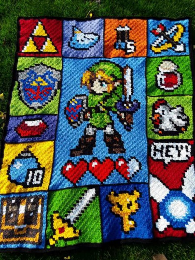 以下が含まれることがあります： ゼルダの伝説のビデオゲームシリーズから、さまざまなピクセル化されたキャラクターとオブジェクトをフィーチャーした、かぎ針編みの毛布。毛布は、緑、青、赤、黄、白など、さまざまな色で作られています。キャラクターとオブジェクトには、リンク、剣、ハート、爆弾、盾、トライフォースが含まれます。