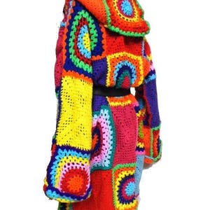 May include: A vibrant, handmade crochet coat featuring a patchwork design in a spectrum of colors including red, orange, yellow, green, blue, and purple. The coat has a hood and long sleeves, with a black belt at the waist.