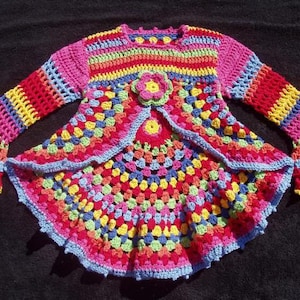 May include: A colorful crocheted cardigan with a rainbow pattern and bell sleeves. The cardigan has a scalloped hem and a flower detail on the front.