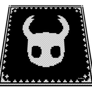 Op de afbeelding: Zwart-witteken met een gepixeld beeld van een gezicht met hoorns en grote ogen. Deken heeft een zwarte rand met witte kruis- en streepjespatronen. Het ontwerp doet denken aan een videogame.