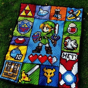 以下が含まれることがあります： ゼルダの伝説のビデオゲームのリンクのピクセルデザインを施した、かぎ針編みの毛布。毛布は緑、青、赤、黄、白の糸で作られています。デザインには、リンクの剣、盾、ハートが含まれています。