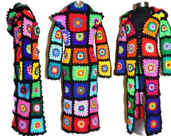 May include: A long, hooded cardigan crocheted in a patchwork pattern of colorful squares. The cardigan has a black background with squares in shades of red, orange, yellow, green, blue, purple, and pink. The cardigan is tied with a black ribbon at the front.