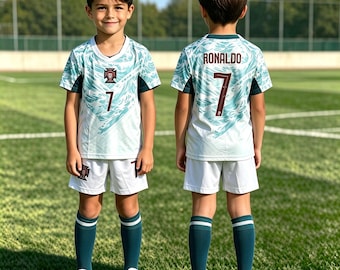 May include: A football kit comprising a white jersey with a teal abstract pattern, the number 7, and a crest on the front. The back displays the name RONALDO and the number 7. The outfit is completed with white shorts and dark teal knee-high socks.