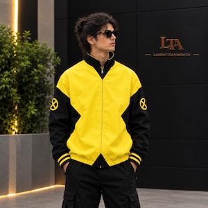 Pode incluir: Um casaco com fecho de correr amarelo e preto com gola alta, mangas compridas com punhos de riscas amarelas e um logótipo X amarelo circular em cada manga. O casaco tem um fecho de correr central e um design com painéis pretos.