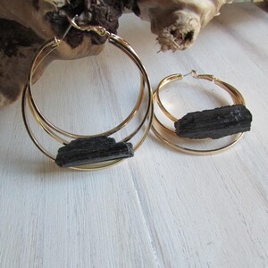 May include: A pair of gold hoop earrings with black tourmaline stones. The earrings are double-hooped and have a simple, elegant design.