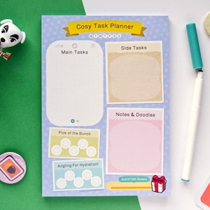 May include: A blue and white planner with the text "Cosy Task Planner" and "MTWTFSS" at the top. The planner has sections for "Main Tasks", "Side Tasks", "Notes & Doodles", "Pick of the Bunch", and "Angling For Hydration!" with spaces for writing and checkboxes. The planner also has a section for "End of Task Reward" with a small illustration of a gift box.