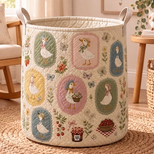 Puede incluir: Una cesta de almacenamiento cilíndrica de tela acolchada color crema con marcos ovalados bordados que contienen ilustraciones de patos con gorros y bufandas, intercalados con motivos florales, mariposas, fresas y un tarro de mermelada.