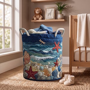 Könnte beinhalten: Ein zylindrischer Wäschekorb aus Stoff mit gestepptem Ozean-Design, verziert mit applizierten Muscheln, Seesternen und einer Libelle. Der Korb hat zwei weiße Seilgriffe und ist mit blauen Stoffstücken gefüllt, die eine Strandlandschaft zeigen.