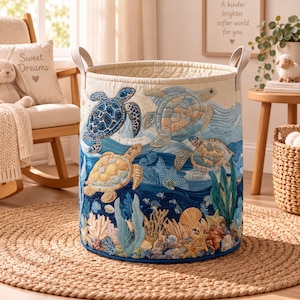 May include: A cylindrical fabric storage basket featuring a quilted texture and an intricate ocean-themed design. The exterior displays embroidered sea turtles, coral reefs, seaweed, and seashells in shades of blue, tan, and cream with two handles.