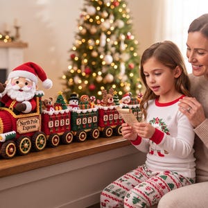 Könnte beinhalten: Ein gehäkelter North Pole Express Adventskalender in Zugform mit einer Weihnachtsmannfigur in der Lokomotive, gefolgt von drei Waggons mit kleinen gehäkelten Weihnachtsfiguren und Geschenken, mit den Zahlen 1 bis 15 an den Seiten.