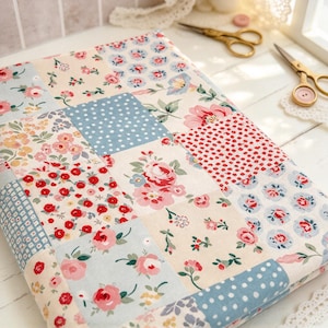 May include: A folded piece of fabric featuring a patchwork design of various floral patterns and polka dots in shades of red, pink, blue, and cream. The textile displays a repeating grid of squares with distinct botanical motifs and geometric prints.