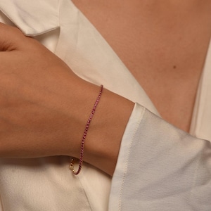 Puede incluir: Una delicada pulsera de tenis con una hilera continua de pequeñas piedras preciosas de color rosa vibrante engastadas en una fina cadena de metal dorado. La pulsera está marcada con 1,82 CT, indicando el peso total en quilates.