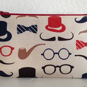 May include: A rectangular cream-colored cosmetic bag with a red zipper and trim. The bag is patterned with navy blue top hats, mustaches, and eyeglasses, along with red bow ties and hats, and brown pipes.