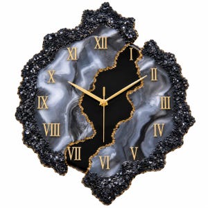 May include: A wall clock with an irregular, geode-inspired shape featuring a black and white marbled face. It has gold Roman numerals, gold hands, and a textured, dark, crystalline border that frames the central marbled design.