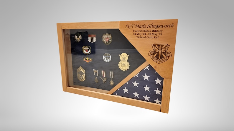 May include: A wooden shadow box display with a framed American flag and a glass display case containing military medals and insignia. The shadow box is engraved with the text "SGT Marie Slingsworth, United States Military, 11 May 13 - 20 May 23, "Defrad Onte Us."