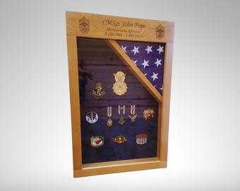 May include: A wooden shadow box with a folded American flag, a purple background, and a variety of military medals and insignia. The text "CMSgt John Pope" is engraved on the top of the box.