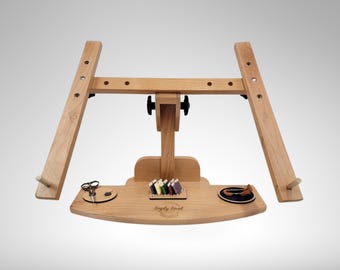 May include: A wooden embroidery stand with adjustable arms, a tray with a compartment for thread, a small dish, and a pair of scissors. The stand is made of natural wood and has a simple, elegant design. The text "Simply Sew" is engraved on the tray.