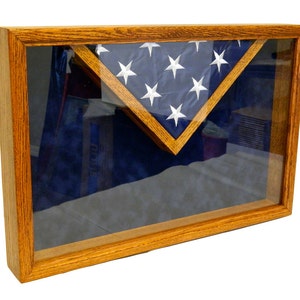May include: A wooden shadow box with a glass front, displaying a folded American flag in a triangular shape on a blue velvet background.