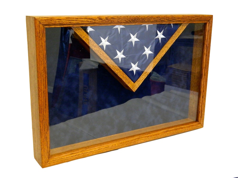 May include: A wooden shadow box with a glass front, displaying a folded American flag in a triangular shape on a blue velvet background.