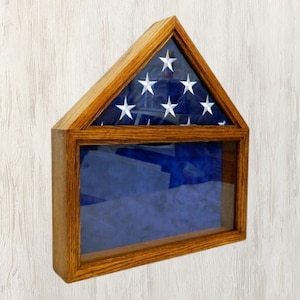 May include: A wooden flag display case with a glass front and a folded American flag inside. The case is shaped like a house and has a dark wood finish.