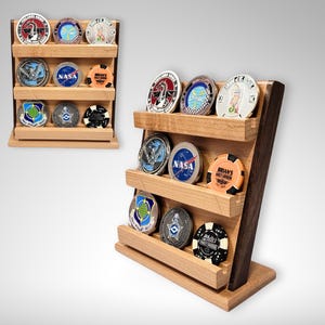 May include: A wooden display stand with three shelves for holding challenge coins. The stand is made of light wood with a dark wood base. The shelves are filled with various challenge coins, including ones with NASA, Air Force, and other designs.
