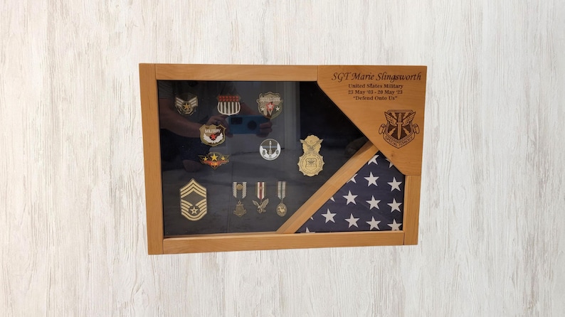 May include: A wooden shadow box with a folded American flag and a display of military medals and insignia. The text "SGT Marie Singaworth United States Military 03 May 92 - 28 May 93 "Devoted Care Co." is engraved on the box.