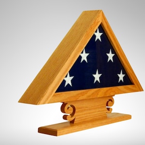 Könnte beinhalten: Ein hölzerner Flaggenständer mit einer gefalteten amerikanischen Flagge im Inneren. Der Ständer ist dreieckig und hat einen Sockel mit dekorativen Schnörkeln.