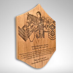 Pu&ograve; includere: Targa in legno con un design inciso al laser. La targa presenta l'immagine di una persona a cavallo, insegne militari e testo. Il testo include un nome, date e una citazione. La targa ha una forma angolare unica.
