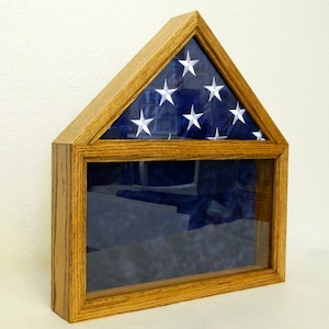 May include: A wooden flag display case with a glass front and a triangular top. The case is made of oak wood and has a dark stain. The case is designed to hold a folded American flag.