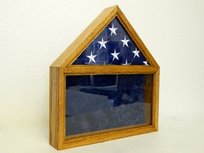 May include: A wooden flag display case with a glass front and a triangular top. The case is made of oak wood and has a dark stain. The case is designed to hold a folded American flag.