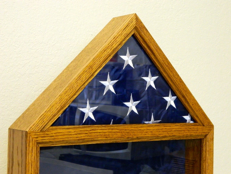 May include: A wooden shadow box with a glass front, displaying a folded American flag. The flag is blue with white stars and is folded in a triangular shape.