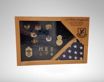 May include: A wooden shadow box with a folded American flag and a display of military medals and patches. The box is engraved with the text "SGT Marie Stingaworth United States Military 01 May 98 - 29 Mar 03 "Defend Our Way" "