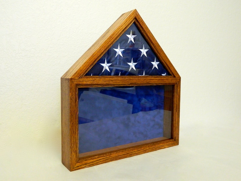 May include: A wooden flag display case with a glass front and a folded American flag inside. The case is stained a dark wood color and has a triangular top.