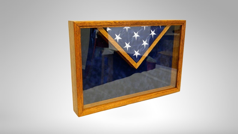 May include: A wooden shadow box with a glass front, displaying a folded American flag. The flag is displayed in a triangular shape with the stars facing outward.