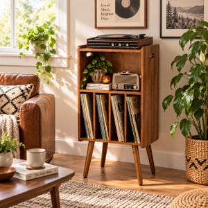 May include: A wooden record player stand with four vertical storage compartments for vinyl records. The top surface holds a black record player, while the middle shelf contains a small potted plant, a candle, and a beige radio.
