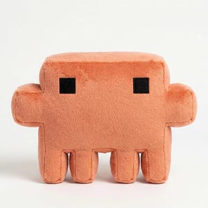May include: A plush toy shaped like a blocky, pixelated creature in a solid peach-orange color. The soft, stuffed figure features a rectangular body, two short arms extending from the sides, and four stubby legs. Two small black squares serve as eyes.