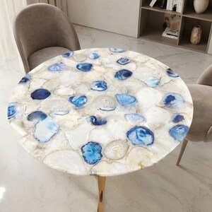May include: A round table featuring a tabletop composed of numerous polished, translucent white and vibrant blue agate stone slices embedded together. The surface displays a mosaic of natural mineral patterns with varying shades of blue.