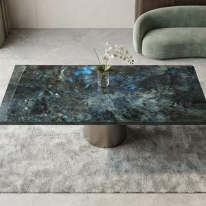 Könnte beinhalten: Ein rechteckiger Couchtisch mit einer polierten Tischplatte aus dunkelblauem und schwarzem Stein mit natürlicher Maserung und irisierenden blauen Akzenten, getragen von einem zylindrischen Metallsockel, mit einer kleinen Glasvase mit weißen Blumen.