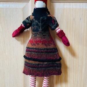 Peut inclure: Poup&eacute;e artisanale avec un grand chapeau pointu bordeaux et des mitaines et bottes assorties. La poup&eacute;e a un col roul&eacute; noir et une robe &agrave; motifs dans les tons de rouge, marron et noir. Les jambes de la poup&eacute;e sont ray&eacute;es rouge et blanc.