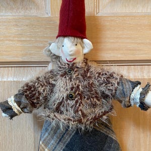 May include: A handmade elf doll with a red hat, brown and white fuzzy jacket, and a plaid skirt.