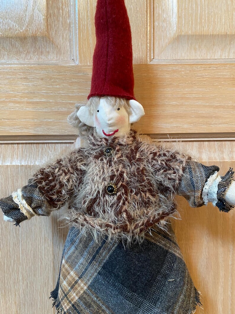 May include: A handmade elf doll with a red hat, brown and white fuzzy jacket, and a plaid skirt.